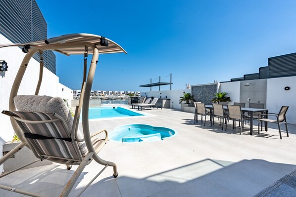 Un espace piscine aménagé sur le toit, avec des chaises longues, une table et une pergola.