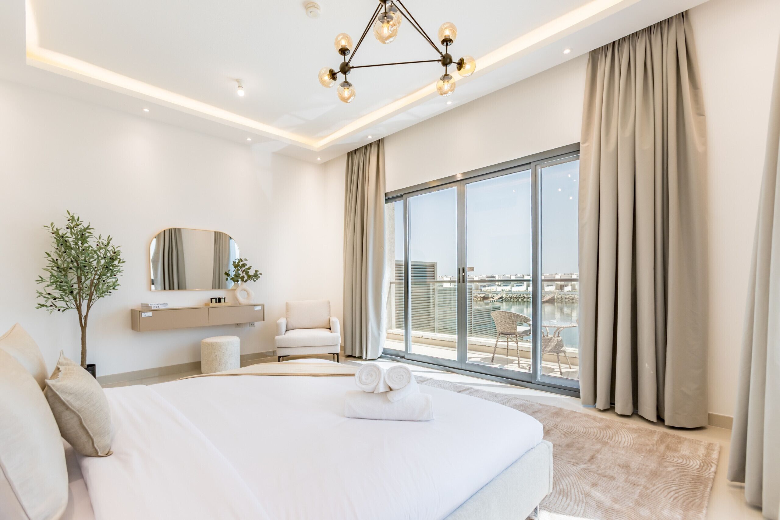 A modern hotel room with a large bed, a seating area, a view of the city, and a ceiling light fixture.