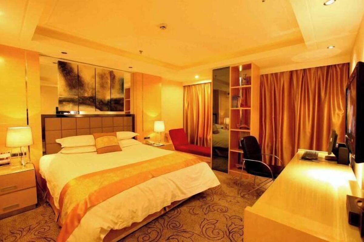 A hotel room with a large bed, a desk, a chair, a wardrobe, and a mirror.