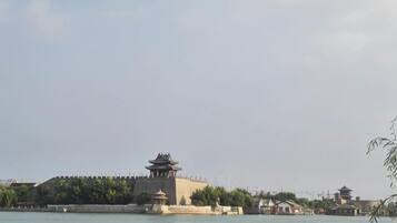 A traditional building with a pagoda-style roof, a large open space in front, and a body of water.