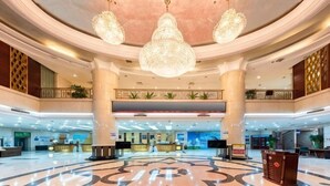 Un vestíbulo amplio con un diseño circular central, varias recepciones y un techo alto con candelabros.