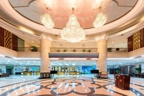 Un'ampia hall con un design circolare centrale, diverse reception e un soffitto alto impreziosito da lampadari.