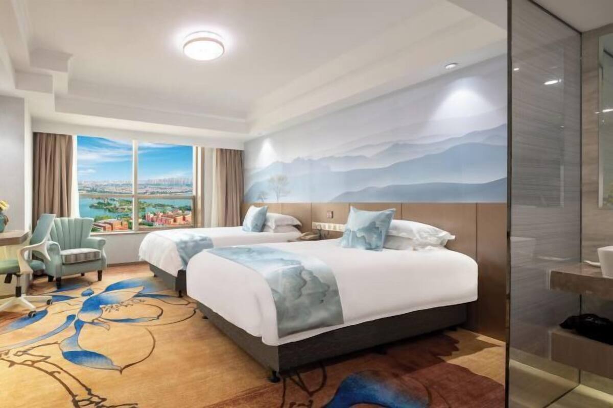 A hotel room with two beds, a large window with a city view, a desk with a chair, and a modern design.
