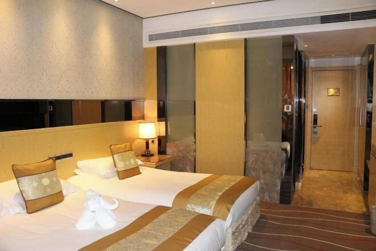 A hotel room with two beds, a nightstand with a lamp, a robe, and a wooden door.