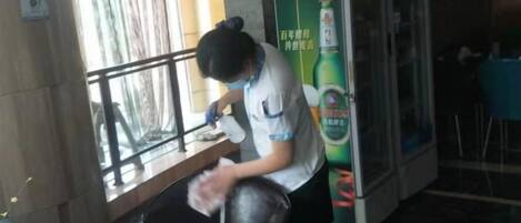 A person cleaning a chair in a room with a window, a refrigerator, and a table.