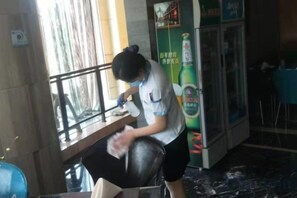 A person cleaning a chair in a room with a window, a refrigerator, and a table. - Liaocheng Yuelu Hotel (Liaocheng)