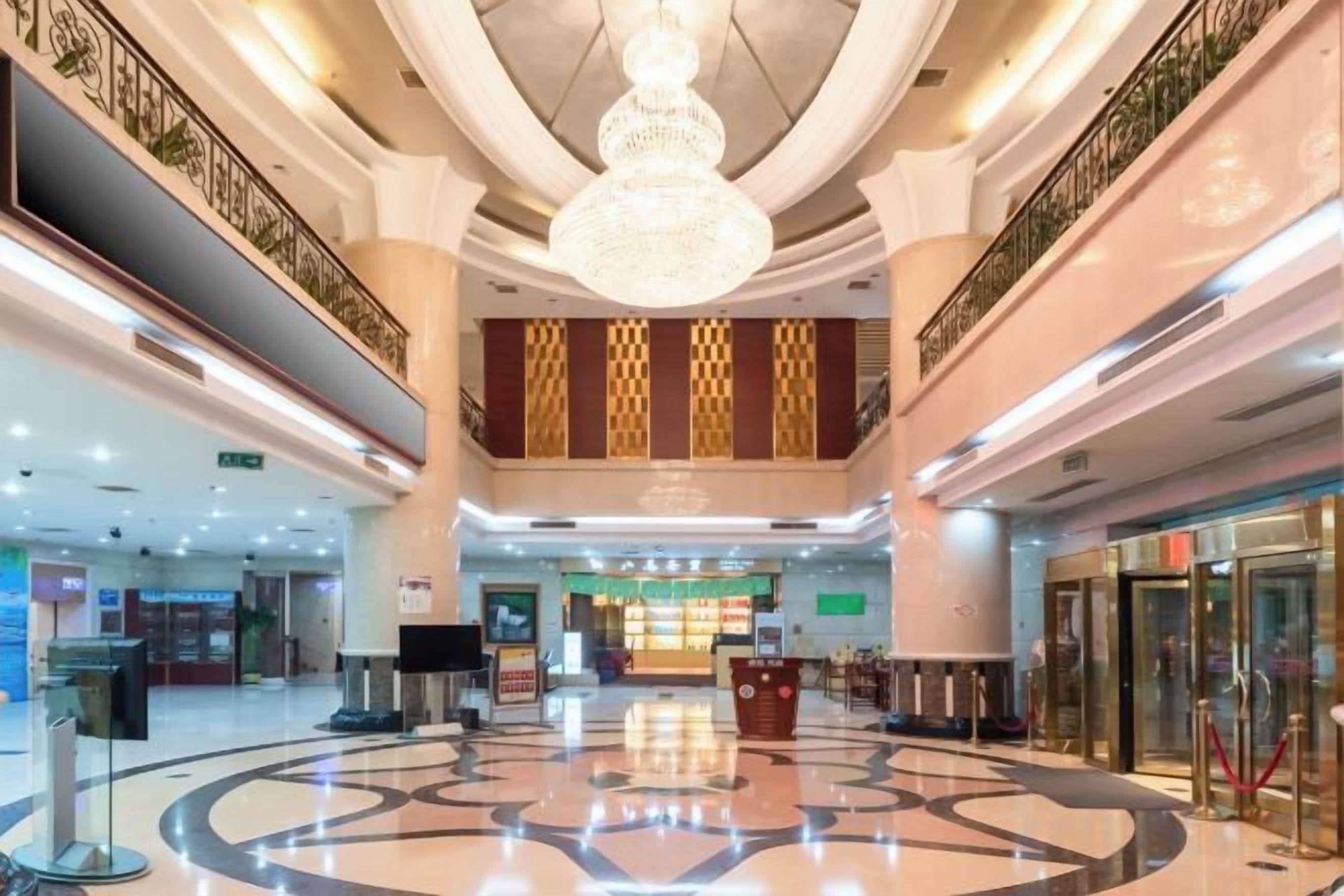 A spacious lobby with a central chandelier, a reception desk, and a check-in counter.