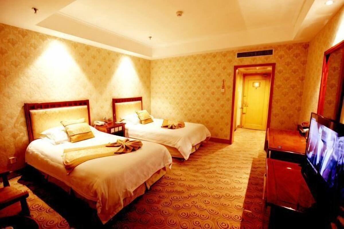 A hotel room with two beds, a TV, and a carpeted floor.