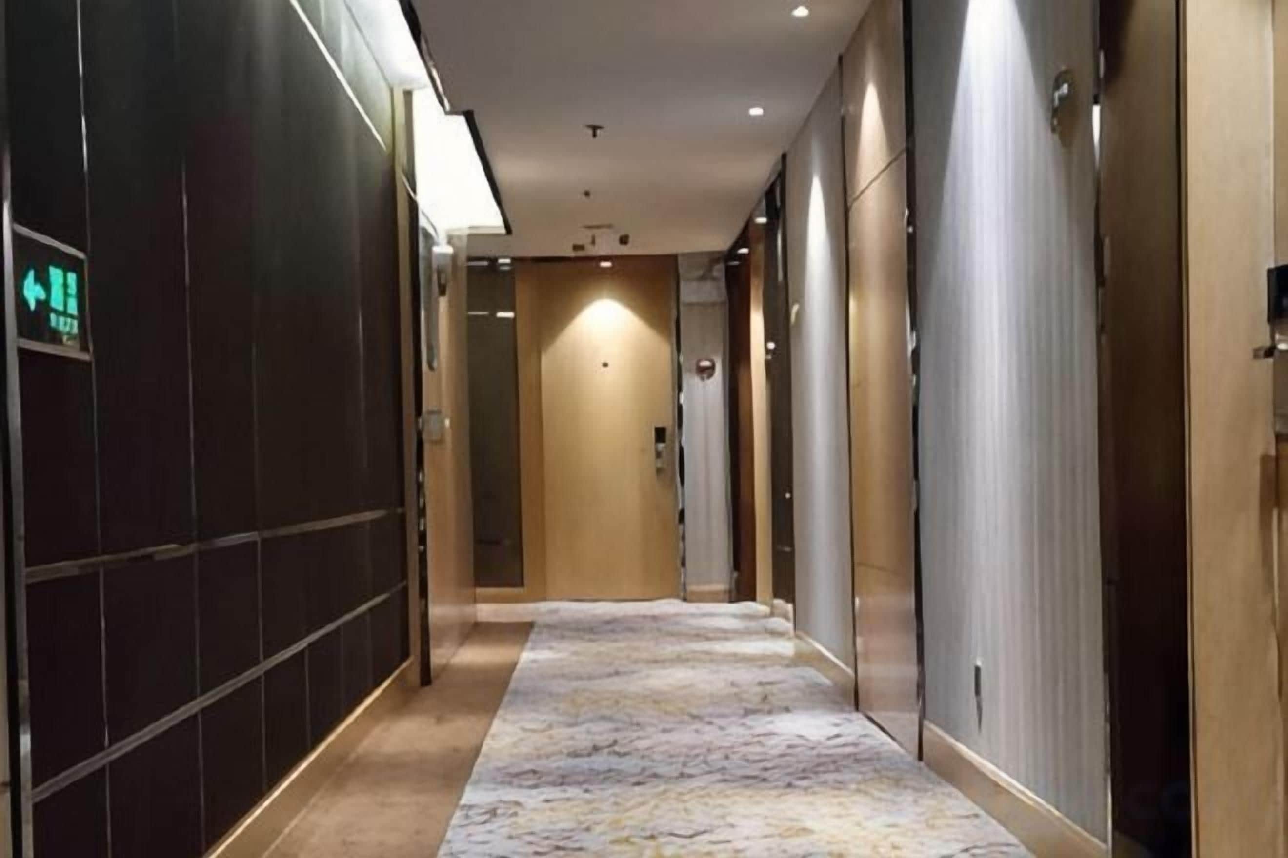 Corredor de hotel com carpete estampado, portas em ambos os lados e uma placa indicando a saída.