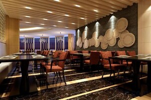 A restaurant with multiple tables and chairs, a patterned wall, and a modern ceiling design.