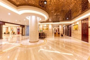 A spacious lobby with a large central column, a reception desk, and a modern ceiling design.