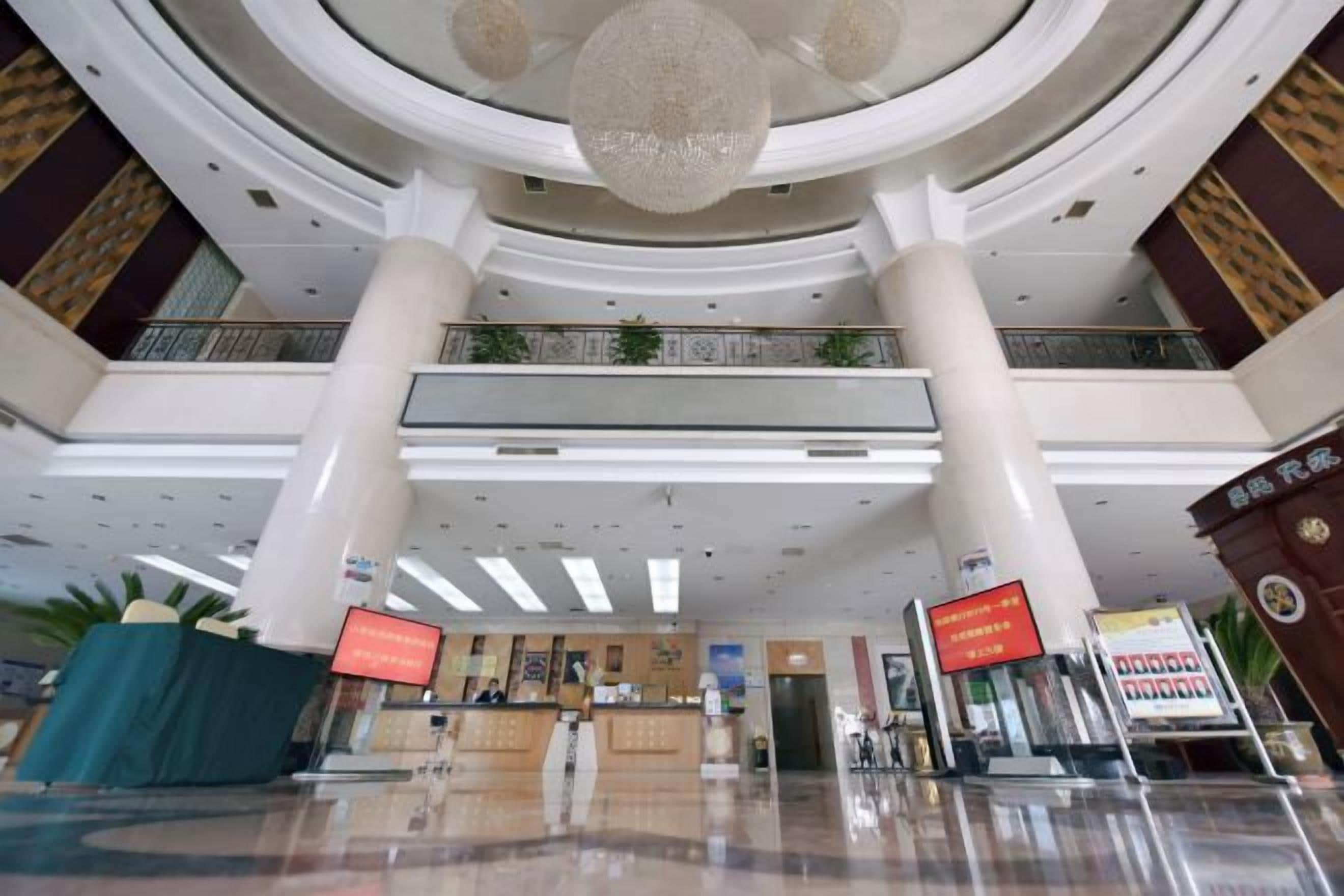 A spacious lobby with a reception desk, a chandelier, and a staircase leading to upper floors.