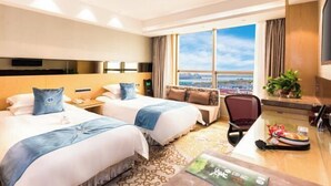 Habitación de hotel con dos camas, un escritorio, una silla, un televisor y un ventanal grande con vista a la ciudad.