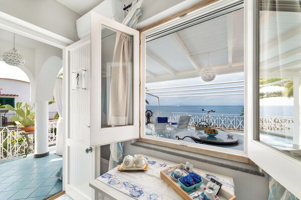 A balcony with a view of the sea, a table with a tray of items, and a chair with a blue towel.
