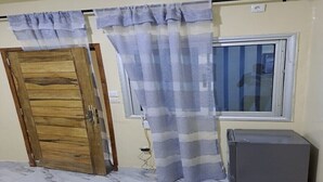 Een kamer met een houten deur, een raam met gordijn en een koelkast.