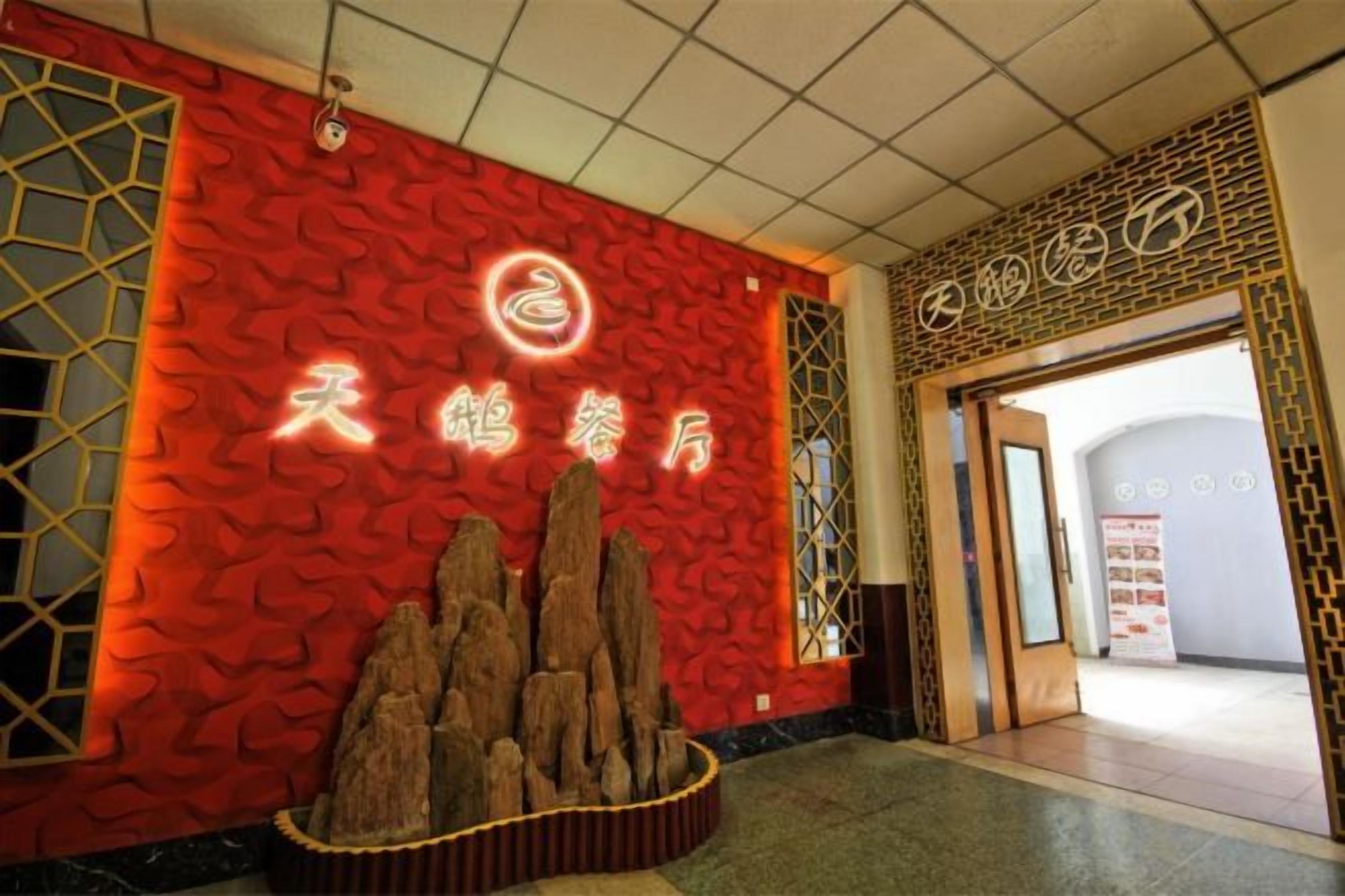 A hotel entrance with a red textured wall, a wooden display of rocks, and Chinese characters.