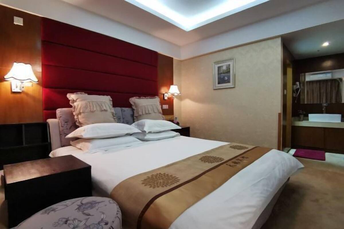 Habitación de hotel con cama, dos lámparas de noche, mesita de noche y un cuadro colgado en la pared, además de una ventana con cortinas.