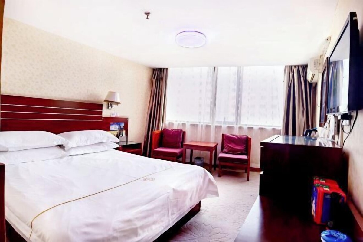 Een hotelkamer met een groot bed, een bureau, een stoel, een televisie en een raam met gordijnen.