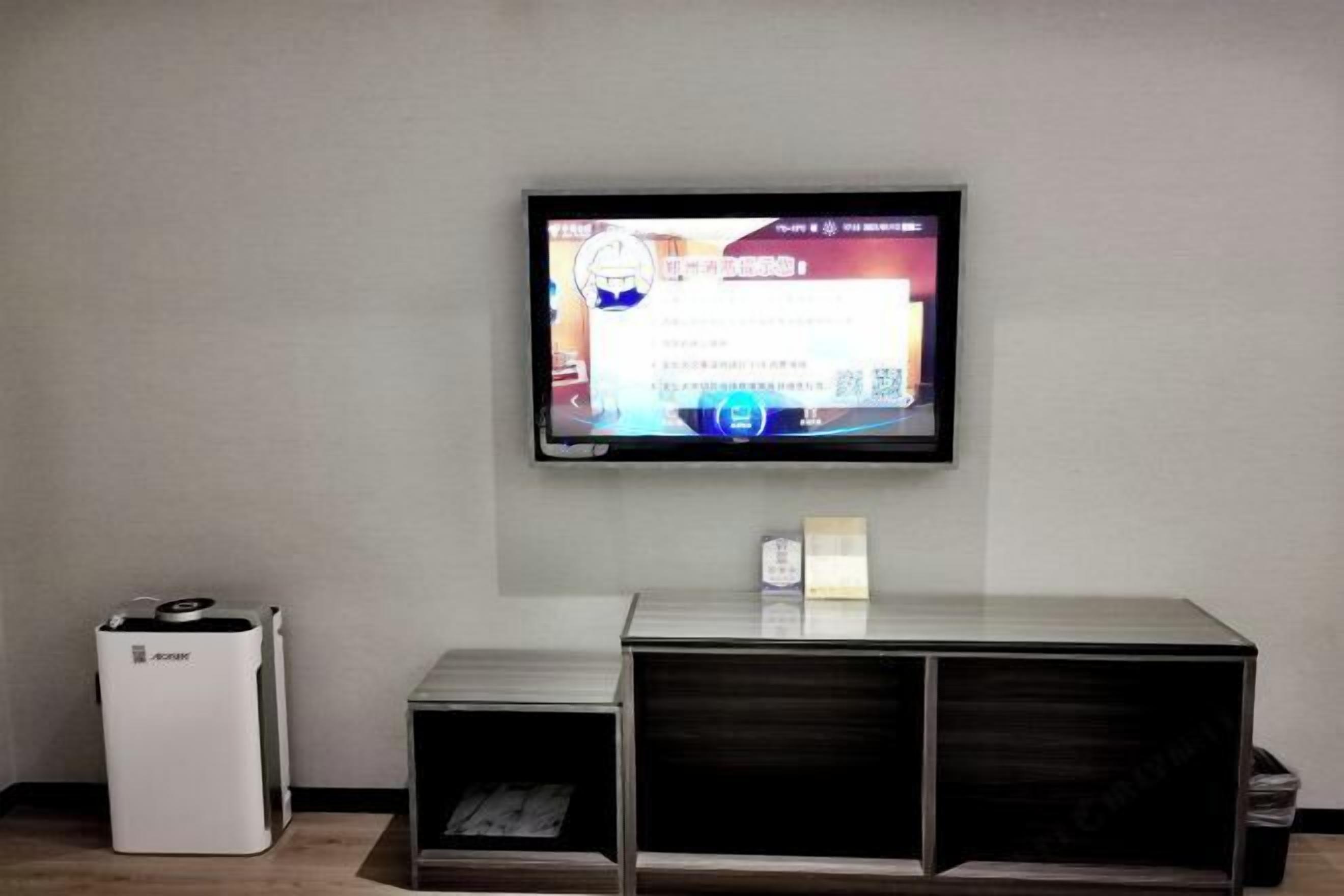 A television mounted on a wall, a white air purifier, and a wooden cabinet below the TV.