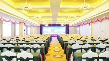 A conference room with rows of white chairs with green sashes, a yellow carpet, chandeliers, and a large screen at the front.