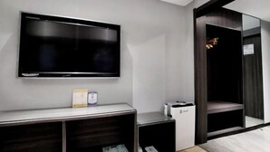 A modern hotel room with a flat-screen TV mounted on the wall, a small desk with a computer, and a large mirror reflecting the room. - Swan Theme Culture Hotel (Zhengzhou Railway Station East Plaza Branch) (Zhengzhou)