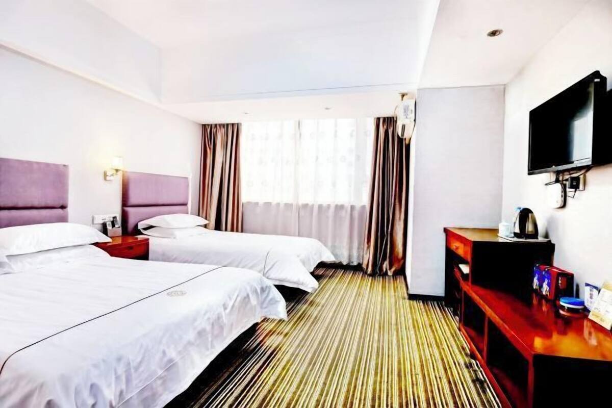 Una habitación de hotel con dos camas, televisión, escritorio y ventana con cortinas.