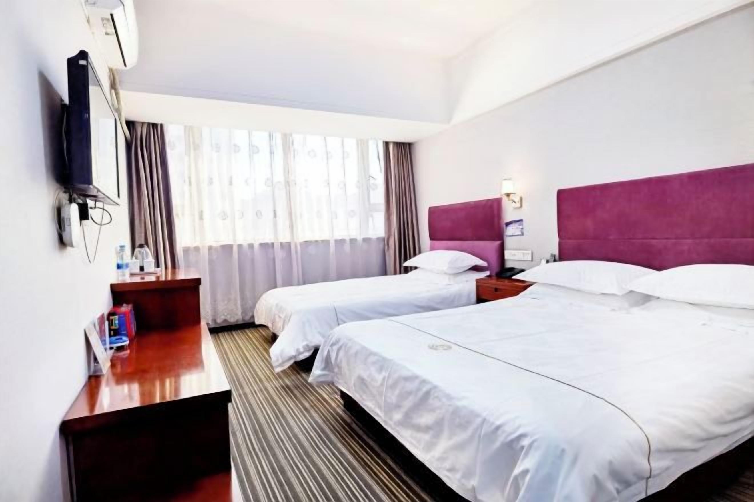 A hotel room with two beds, a desk, a TV, and a window with curtains.