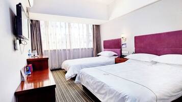 A hotel room with two beds, a desk, a TV, and a window with curtains.