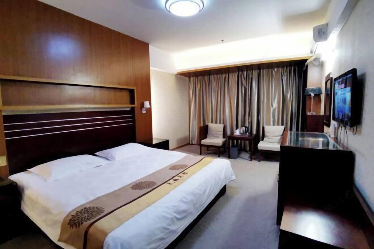 Habitación de hotel con cama, escritorio, silla, televisor y ventana con cortinas.