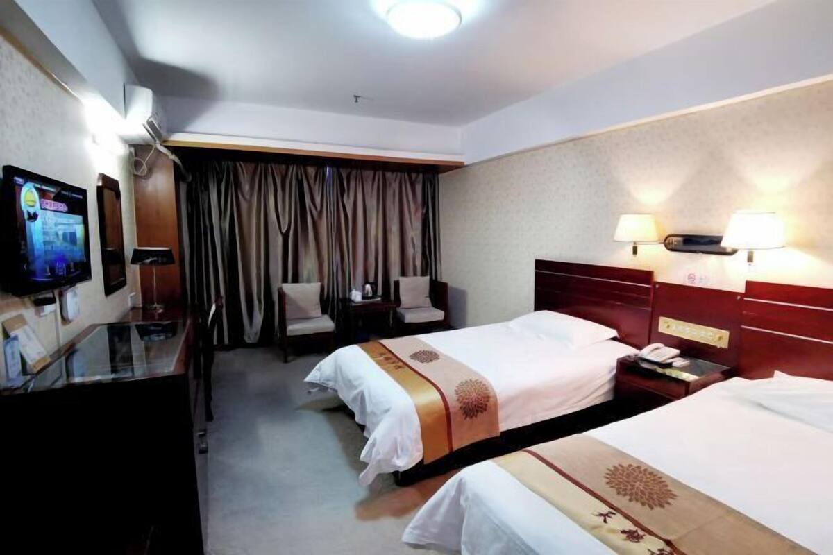 Una habitación de hotel con dos camas, televisión, escritorio con computadora y ventana con cortinas.