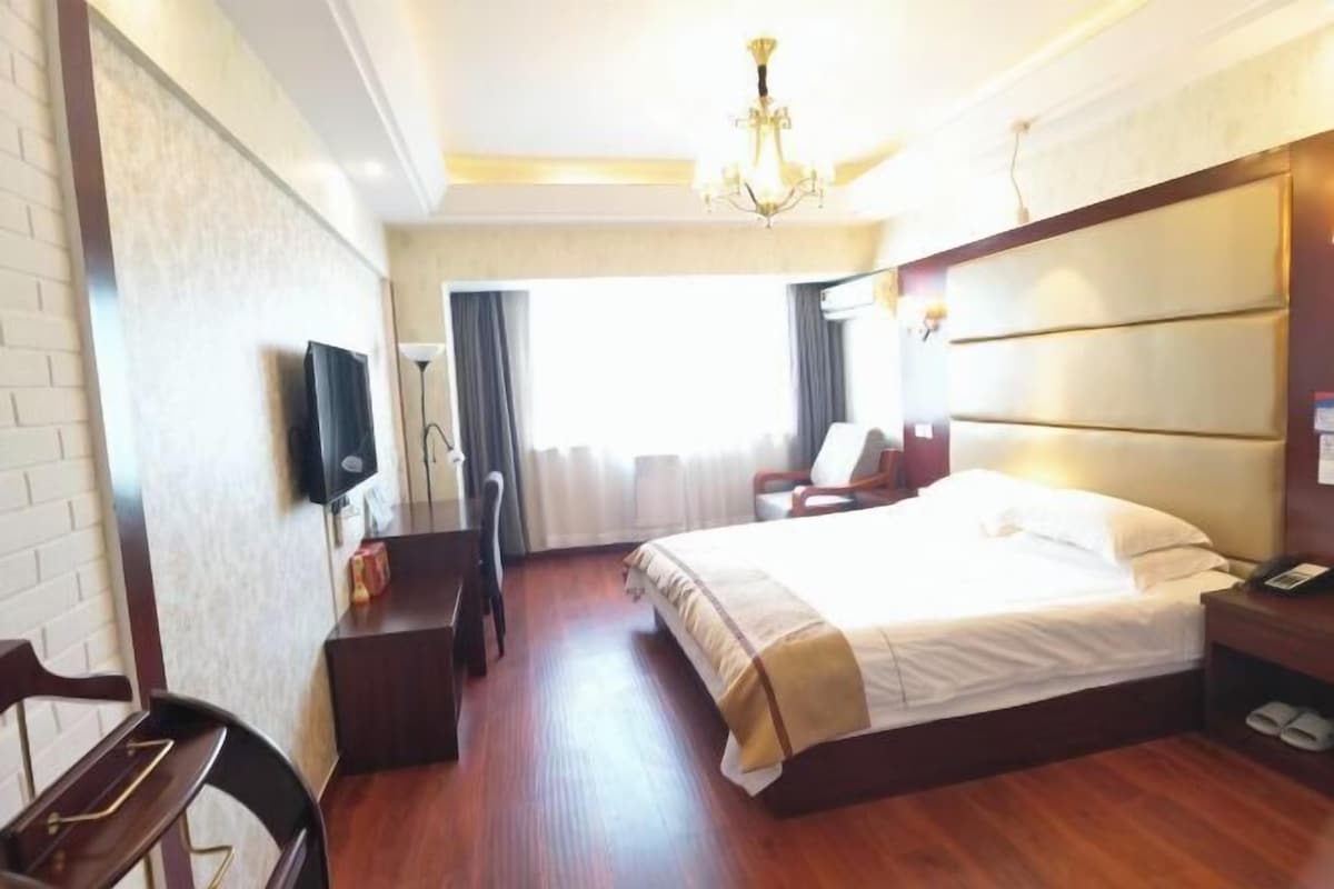 A hotel room with a bed, a desk, a chair, a television, and a window with curtains.