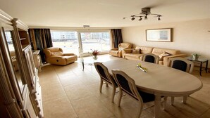 A spacious living room with a large dining table, comfortable seating, and a view of the city through the large windows.