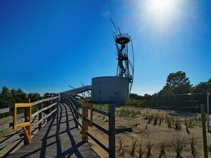 A wooden boardwalk leading to a metal structure with a circular base, surrounded by sparse vegetation and a clear sky. - Apartment in Middelkerke With Sea View (Middelkerke)