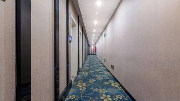 A hotel corridor with a patterned carpet, doors on the left, and a long hallway.