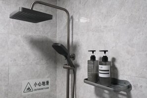 Une douche équipée d’un pommeau de douche à main, d’un robinet mural et d’une étagère sur laquelle sont posés deux flacons de shampoing et d’après-shampoing.