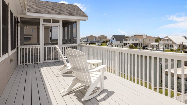 A wooden deck with rocking chairs and a small table, overlooking a body of water and neighboring houses. - Always Sunday-Pet Friendly Home in Atlantic Beach, NC (Atlantic Beach)