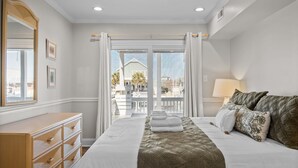 A hotel room with a large bed, a wooden dresser, a mirror, and a view of the outside balcony. - Always Sunday-Pet Friendly Home in Atlantic Beach, NC (Atlantic Beach)