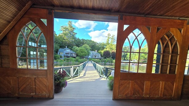 Una terraza de madera con vistas a un puente que lleva a casas rodeadas de vegetación.