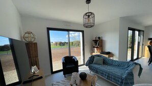 A modern living room with a large TV, a wooden coffee table, a blue sofa, and a view of the outdoors through large sliding doors. - New vacation home 5 minutes from the sea (Plobannalec-Lesconil)
