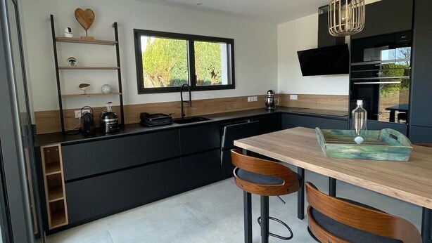 A modern kitchen with a central island, black cabinetry, and a large window. - New vacation home 5 minutes from the sea (Plobannalec-Lesconil)