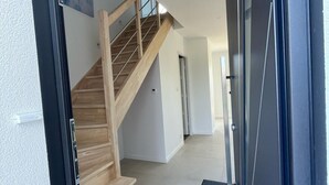 A modern interior with a wooden staircase leading to a second floor, a door with a black frame, and a hallway with a light-colored floor. - New vacation home 5 minutes from the sea (Plobannalec-Lesconil)