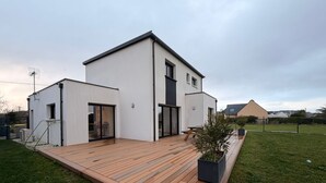 A modern two-story house with a wooden deck, large sliding glass doors, and a small garden area. - New vacation home 5 minutes from the sea (Plobannalec-Lesconil)