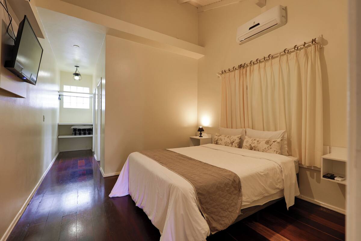 A bedroom with a bed, a nightstand, a TV mounted on the wall, and a window with curtains.