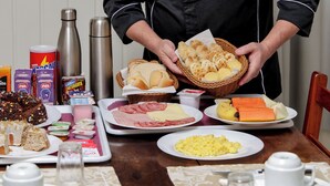 A chef presenting a basket of bread to a table set with various breakfast items. - Pousada Maison Suisse  (Canela)