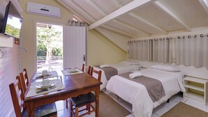 A room with a wooden dining table set for two, two single beds with white bedding, a TV mounted on the wall, and a window with curtains. - Pousada Maison Suisse  (Canela)