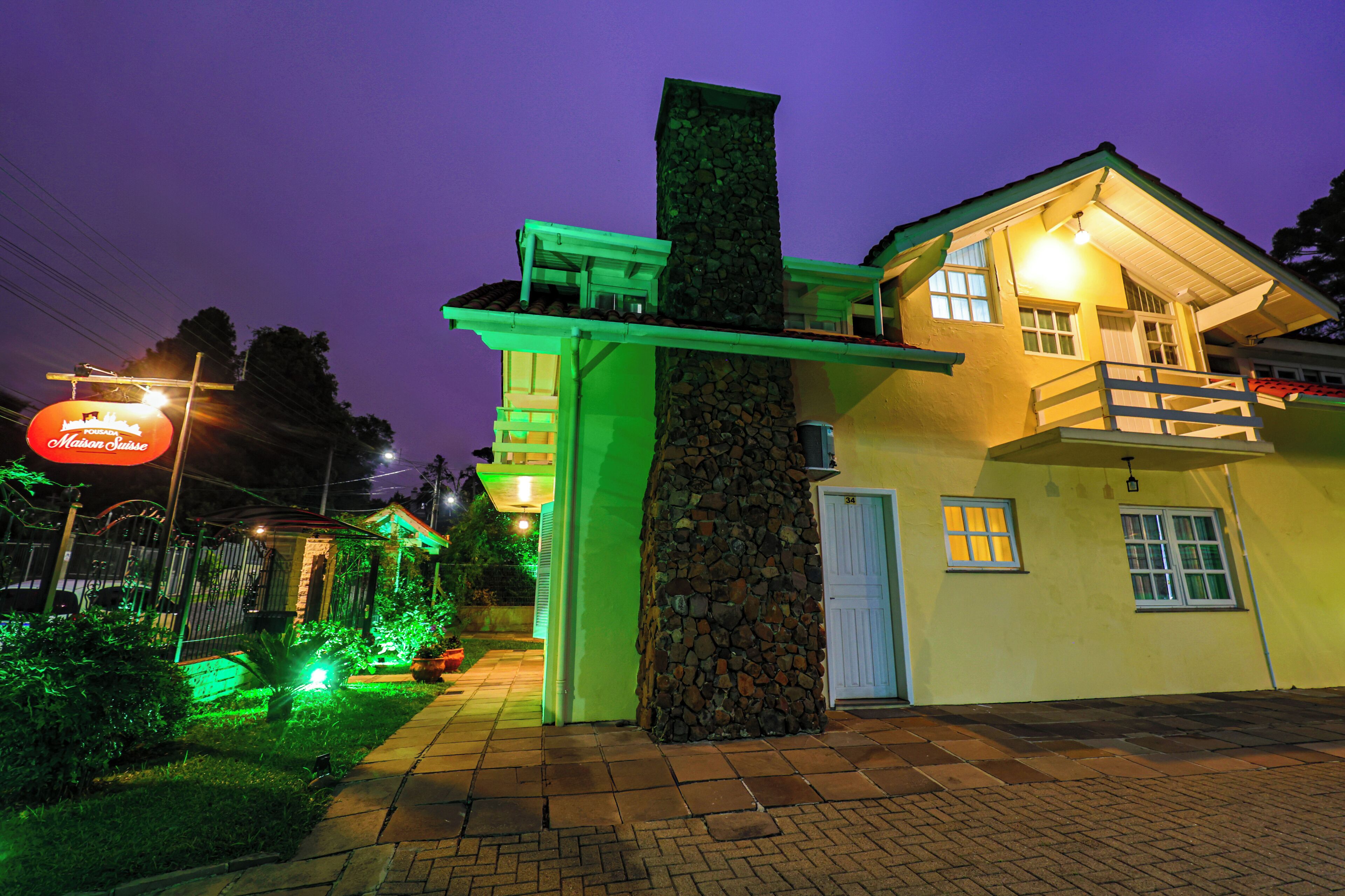 Un edificio de dos pisos con chimenea de piedra, un balcón y un letrero iluminado.