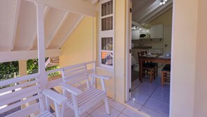 A balcony with white railings and a bench, a kitchen area with wooden cabinets and a dining table, and a view of greenery outside. - Pousada Maison Suisse  (Canela)