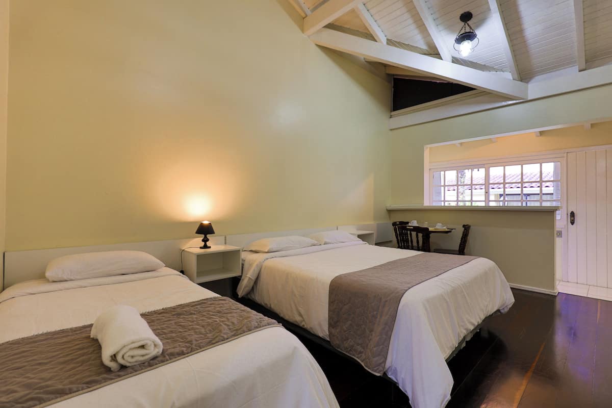 A hotel room with two beds, a nightstand, a table with chairs, and a window with a view of buildings.