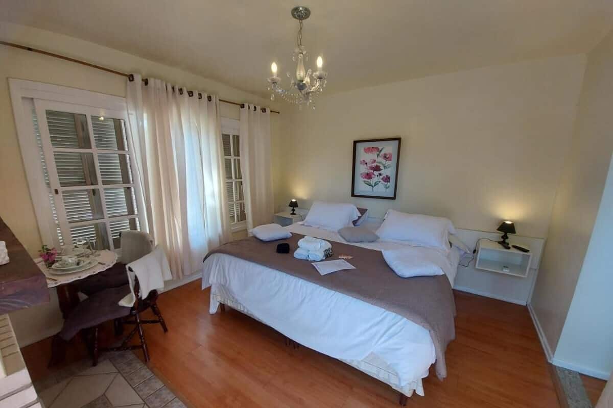 A bedroom with a bed, bedside tables, a desk, and a chandelier.