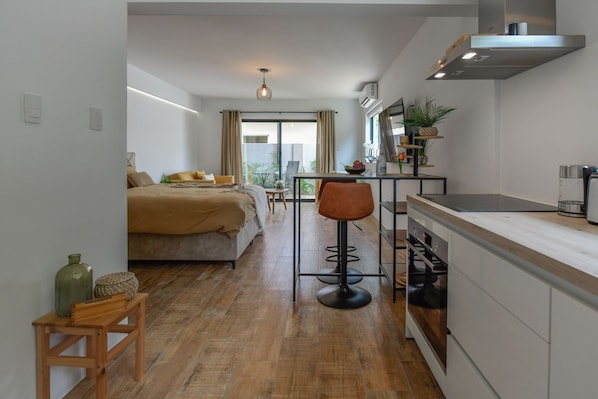 A modern hotel room with a bed, a small dining table, a kitchen area, and a view of the outdoors. - 50m2 NEW condo Oranjestad - Rated 10/10 & 5-star - Arubaislanderresidence.com (Oranjestad)